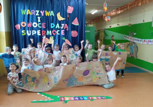 Dzieci z grupy Skoczki prezentują własnoręcznie wykonane plakaty wykonane farbami plakatowymi, które zachęcają dzieci do jedzenia owoców i warzyw.