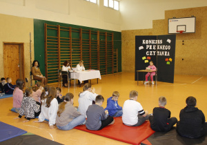 Uczniowie siedzą na materacach i słuchają czytanego tekstu. Pani Dyrektor Szkoły i członkowie komisji słuchają. Uczennica kl. IV czyta.