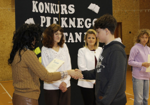 Pani Dyrektor wręcza dyplom uczniowi kl. VI za udział w Konkursie. Za nim stoi nauczyciel bibliotekarz i polonistka Szkoły. Obok stoi uczennica kl. V i trzyma w ręku dyplom.