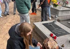 Uczniowie klasy VII b sprzątają cmentarz, uczennice SU zapalają znicze.