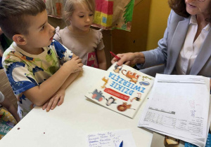 Przedszkolaki ze Szkoły Filialnej w Sadykierzu kupują książki. Pani bibliotekarka sprawdza cenę książki ,,Dzikie zwierzęta”.