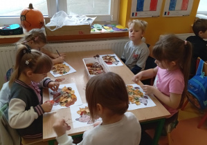 Dzieci z grupy Skoczki wyklejają jeża z jesiennych liści.
