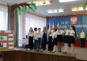 Uczniowie w galowym stroju śpiewają piosenkę pt:„Wojenko, Wojenko”.