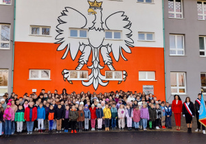 Uczniowie klas I - VIII wraz z Panią Dyrektor i Sztandarem Szkoły stoją przed szkoła i śpiewają hymn polski.