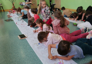 Uczniowie na korytarzu kolorują kredkami i markerami malowankę.