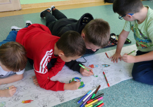 Chłopcy kolorujący kredkami świecowymi malowankę.