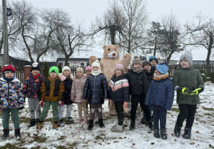 Grupowe zdjęcie dzieci z pluszowym misiem.