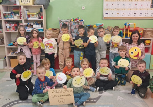 Przedszkolaki z grupy Zuchy prezentują swoje prace na dywanie w sali obok jest pedagog specjalny.