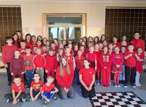 Uczniowie klas I - VIII wraz z Panią Dyrektor oraz psychologiem i pedagogiem specjalnym stoją lub niektórzy siedzą w korytarzu szkolnym.