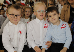 Trzech przedszkolaków ubranych na galowo z przypiętymi kotylionami.