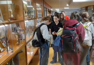 Uczniowie stoją przy gablocie z pucharami.