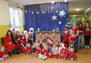 Grupa Zuchy na tle świątecznej dekoracji ze św. Mikołajem, panią Dyrektor Agatą Ewą Ostalską i Zastępcą Wójta panią Iwoną Łuszcz-Krawczyk.