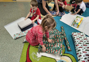 Dzieci z grupy Słoneczka zawijają pudełka w kolorowy świąteczny papier.