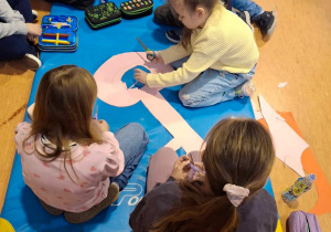 Uczniowie siedzą na materacu i wycinają klucz z papieru.