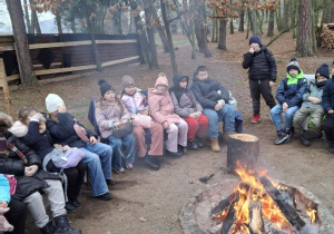 Dzieci siedzą przy ognisku.