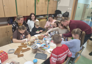 Dorośli pomagają dzieciom dekorować pierniki.