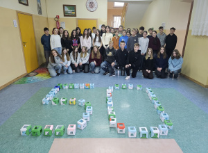 Uczniowie klas siódmych na szkolnym korytarzu. Przed uczniami ułożona jest "pięćdziesiątka" z pięćdziesięciu sześcianów modułowych.