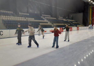 Uczniowie jeżdżą na łyżwach na torze łyżwiarskim.