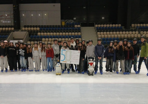 Uczniowie stoją na lodzie i trzymają plakat okolicznościowy z okazji 50 lecia.