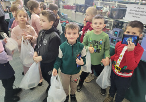 Uczniowie trzymają w ręku swoje torebki z zakupionymi bombkami.
