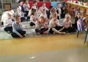 Dzieci z grupy Zuchy siedzą na dywanie i śpiewają kolędy.