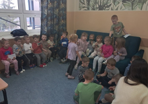 Przedszkolaki siedzą na kanapie oraz ławce w szkole i jedzą zakupione słodkości oraz owoce.