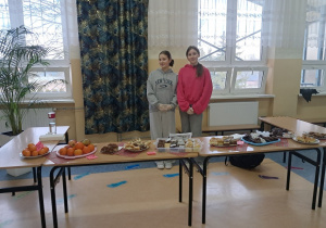 Uczennice z Samorządu Uczniowskiego gotowe do sprzedaży słodkości na korytarzu szkolnym.