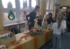 Uczniowie kl. VIII a sprzedają na korytarzu szkolnym ozdoby bożonarodzeniowe.