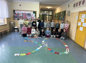 Uśmiechnięci uczniowie wraz z nauczycielem prezentują swoje prace.