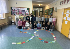 Uśmiechnięci uczniowie wraz z nauczycielem prezentują swoje prace.