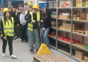 Uczeń obsługuje żółty wózek paletowy z paletą.