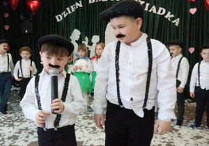 Chłopcy w czapkach dziadka i z wąsami pod nosem.