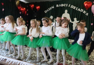 Dziewczynki w zielonych spódniczkach tańczą.