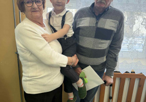 Dziadkowie trzymają wnuka na rękach.