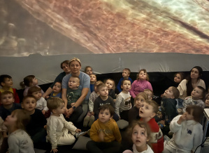Przedszkolaki z grupy Kamyczki, Szkraby i Skoczki w trakcie oglądania seansu o dinozaurach w mobilnym kinie.