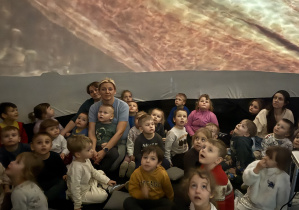 Przedszkolaki z grupy Kamyczki, Szkraby i Skoczki w trakcie oglądania seansu o dinozaurach w mobilnym kinie.