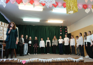 Bibliotekarka szkolna opowiada o Julianie Tuwimie. Na scenie stoją przygotowani do występu uczniowie.