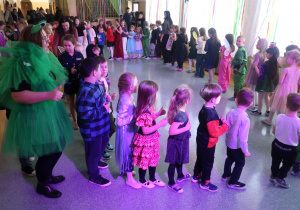 Uczniowie z nauczycielami na korytarzu szkolnym tańczą w kółku podczas balu karnawałowego.