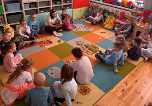 Przedszkolaki z grupy Promyczki siedzą na dywanie i słuchają bajek czytanych przez nauczyciela.