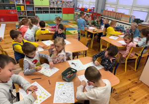 Dzieci z grupy Promyczki siedzą przy stolikach i malują kredkami kolorowankę.
