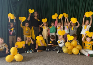 Dzieci z oddziału przedszkolnego z żółtymi sercami i balonami deklarują, że nie są obojętni na potrzeby innych.