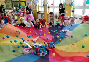 Przedszkolaki z grupy Szkraby podczas zabawy chustą klanza podrzucają kolorowe piłeczki.
