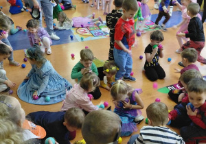 Przedszkolaki zbierają na korytarzu kolorowe piłeczki w czasie zabawy choinkowej.