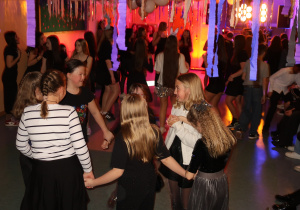 Na pierwszym planie uczennice klasy IV tańczą w kółku trzymając się za ręce.