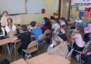 Dzieci z zainteresowaniem słuchają opowieści przedstawionej za pomocą ilustrowanych kart wsuwanych do drewnianej skrzynki – „magicznego okienka".