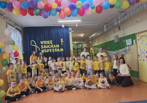 Przedszkolaki z grupy: Zuchy, Krasnale i Promyczki wraz z Ciociami oraz pedagogiem specjalnym stoją na korytarzu przedszkolnym prezentują żółte stroje.