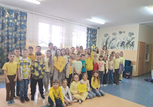 Uczniowie klas I- VII na szkolnym korytarzu wraz z pedagogiem specjalnym prezentują żółte ubrania.