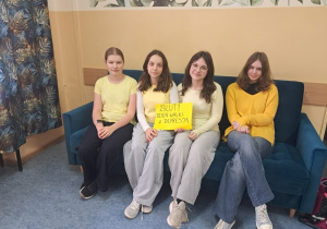 Uczennice klasy VII a i VII b siedzą na kanapie w żółtych ubraniach, uczennice trzymają w ręku napis 23 luty Światowy Dzień Walki z Depresją.