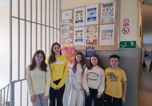 Uczennice z klas VI i VII prezentują swoje żółte stroje obok gazetki szkolnej .