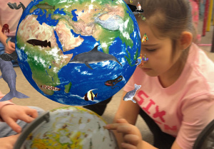 Dziewczynka pokazuje na globusie zwierzątko które pływa w oceanie.